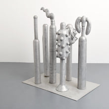 Load image into Gallery viewer, Carol K. Brown (b. 1945 - ) Untitled Sculpture: Six Vertical Elements., 1986 Aluminum Sculpture 53h x 48w x 30d inches Carol K. Brown is a visual artist based in Miami and New York. She began her career as a sculptor, but her work has evolved through numerous phases: anthropomorphic abstractions, figurative paintings, and social commentary. This aluminum statue is composed of six separate pieces on an aluminum base. Available at Manolis Projects Gallery.